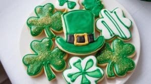 Plate of St. Patrick’s Day Sugar Cookies decorated with green and white icing, featuring shamrock shapes and a leprechaun hat with a yellow buckle.