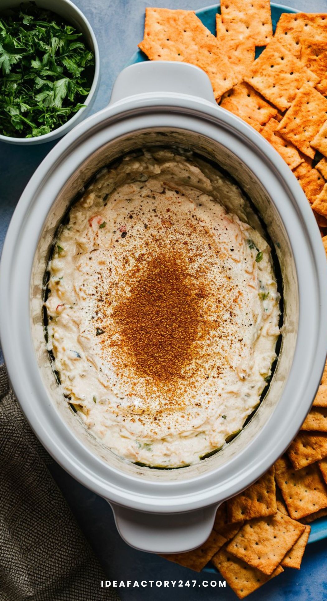 A crockpot of creamy crab dip, topped with a sprinkle of Old Bay seasoning and served with crispy crackers on the side.