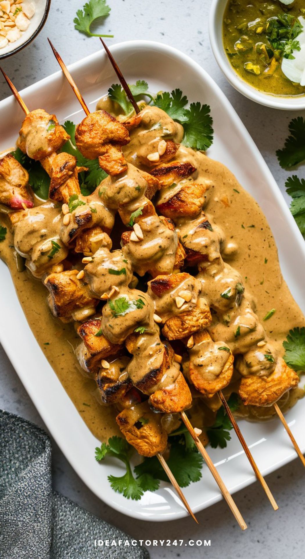 Tender chicken skewers drizzled with creamy peanut sauce, garnished with crushed peanuts and cilantro, served on a white platter.