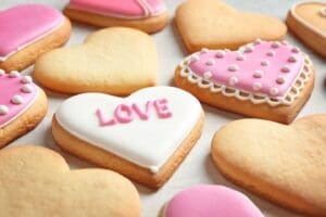 Heart-shaped Valentine’s Day Cookies decorated with pink and white icing, some featuring patterns and one with the word LOVE. The cookies are arranged on a light surface, perfect for celebrating the sweetest day of the year.
