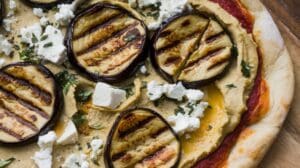 Close-up of a Grilled Eggplant and Hummus Pizza topped with crumbled feta, chopped herbs, and a creamy spread on a golden-brown crust.