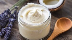 A jar of fluffy, whipped magnesium body butter with a creamy texture, surrounded by ingredients like shea butter, coconut oil, and a small dish of magnesium flakes. A sprig of lavender and a wooden spoon add a natural, spa-like vibe.