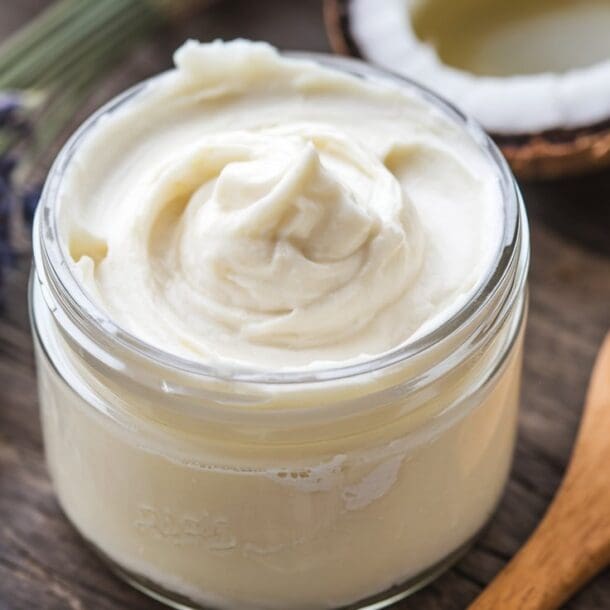 A jar of fluffy, whipped magnesium body butter with a creamy texture, surrounded by ingredients like shea butter, coconut oil, and a small dish of magnesium flakes. A sprig of lavender and a wooden spoon add a natural, spa-like vibe.