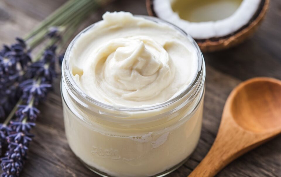 A jar of fluffy, whipped magnesium body butter with a creamy texture, surrounded by ingredients like shea butter, coconut oil, and a small dish of magnesium flakes. A sprig of lavender and a wooden spoon add a natural, spa-like vibe.