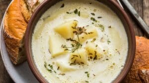 A bowl of creamy Irish Potato Soup Recipe garnished with herbs, served with slices of rustic bread on a plate.