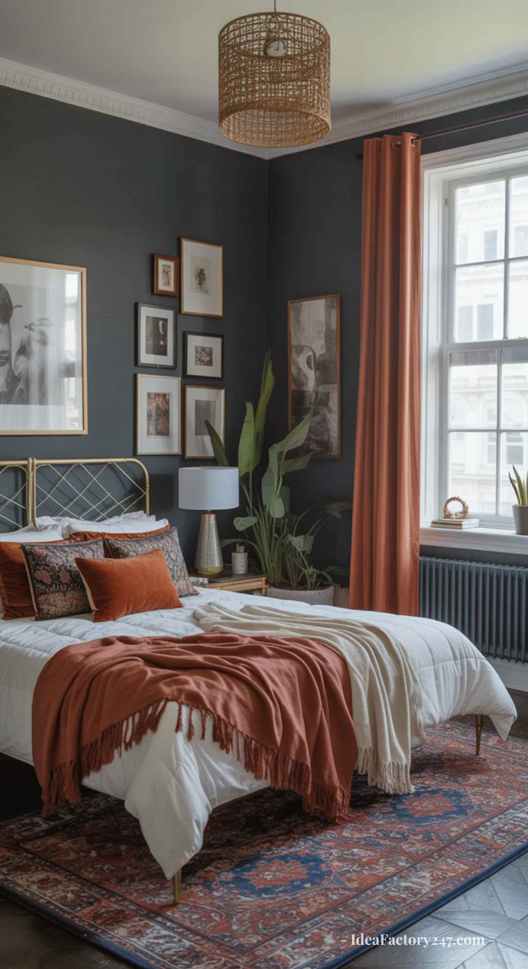 A cozy dark boho bedroom with deep-toned walls, a large window, rust-colored curtains, a gold bed frame, layered pillows, a throw blanket, plants, and framed art on the walls. Natural light brightens the space.