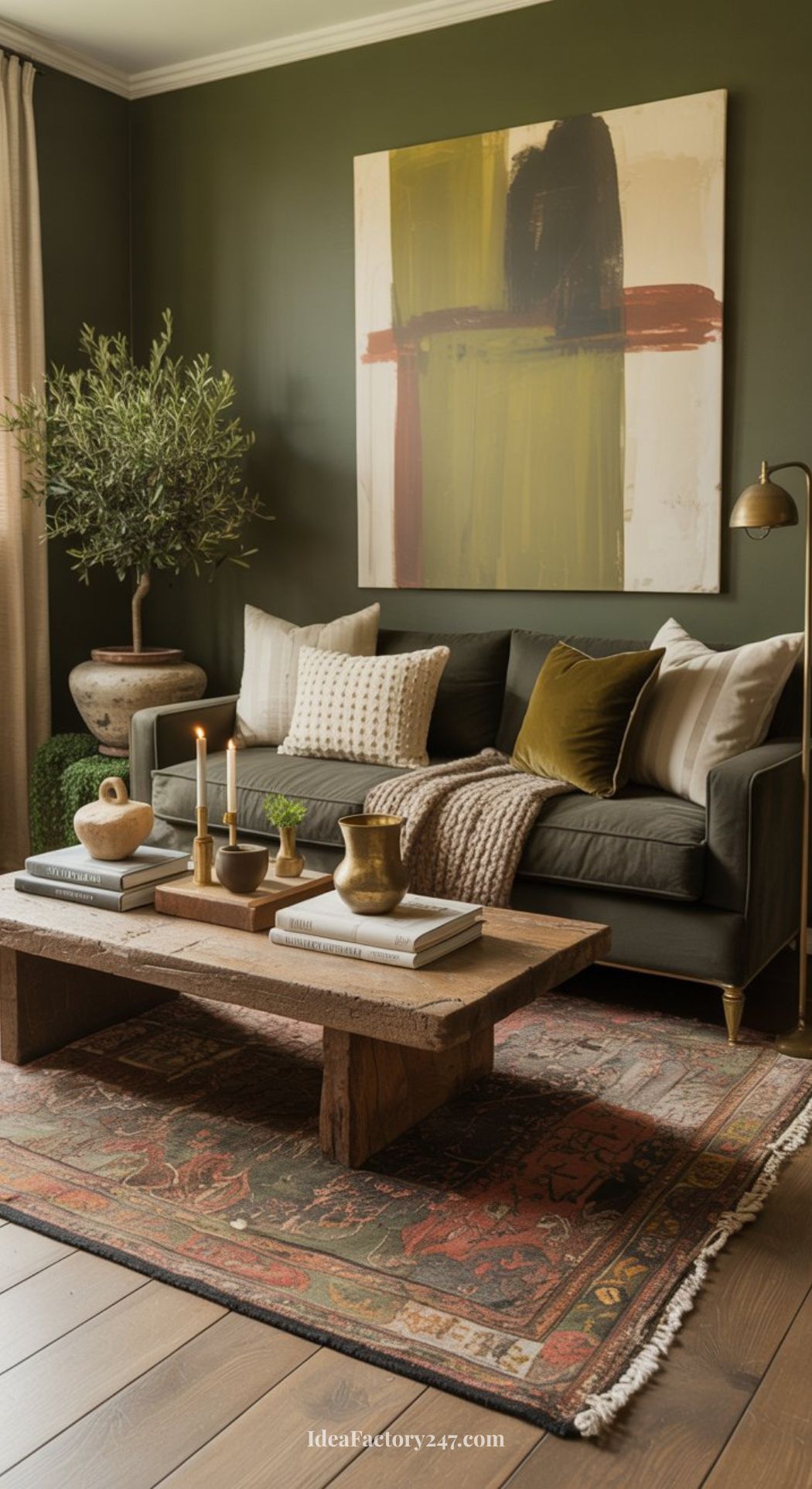 A cozy, earthy living room with an olive green wall, abstract art, a green sofa with pillows, potted plant, rustic wooden coffee table with candles and decor, and a vintage patterned rug on wood flooring.