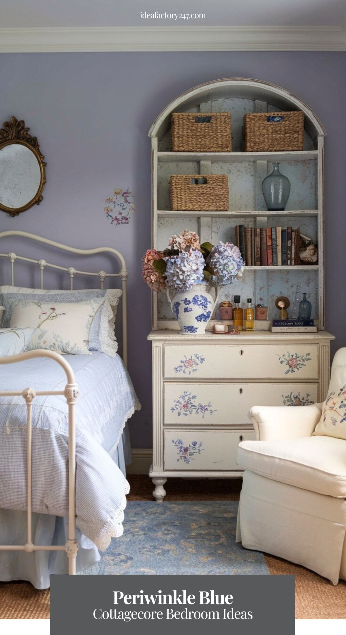 A dreamy periwinkle blue and cream cottage bedroom featuring a softly curved iron bedframe with lace-trimmed bedding in soft blues and whites. The walls are painted a muted lavender-blue, while an antique gold mirror with floral detailing hangs above the bed.
