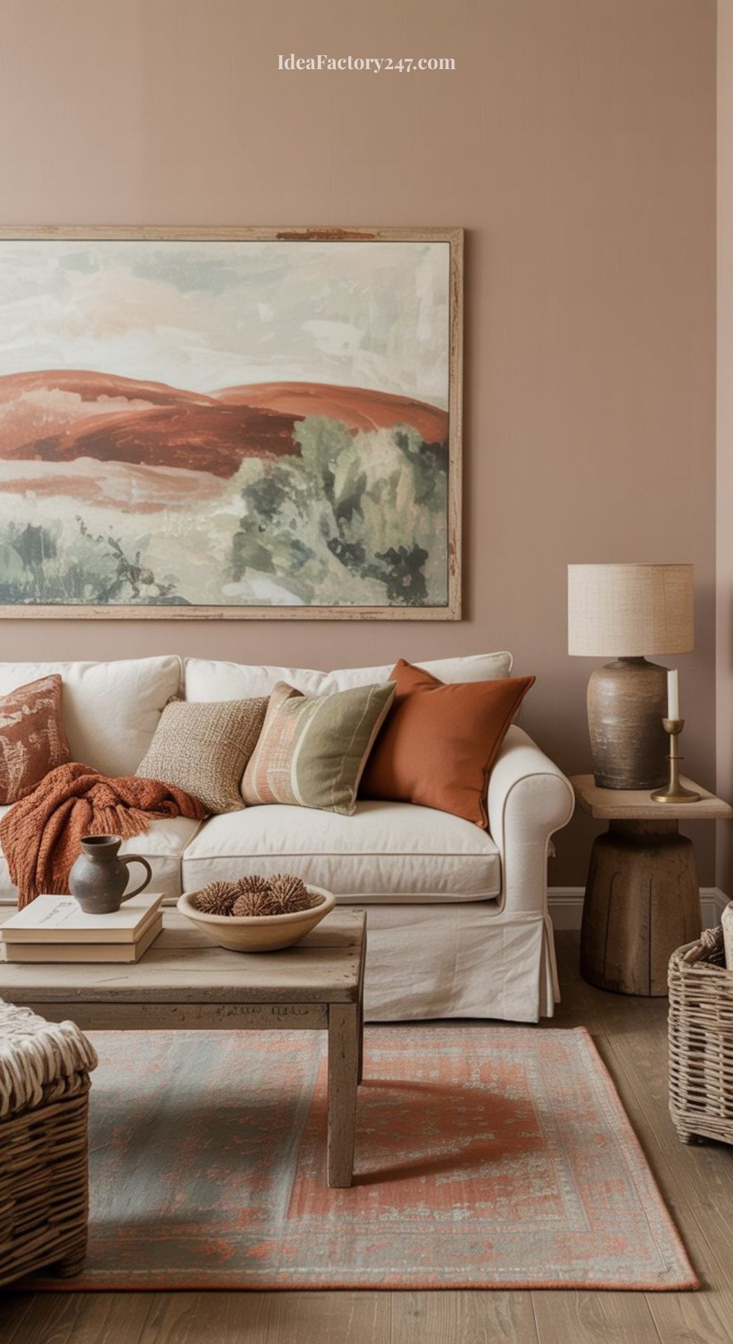 A cozy, earthy living room with a white sofa, earth-toned pillows and blanket, a wooden coffee table, table lamp, woven basket, and warm landscape art on a blush wall. The natural décor creates an inviting retreat.