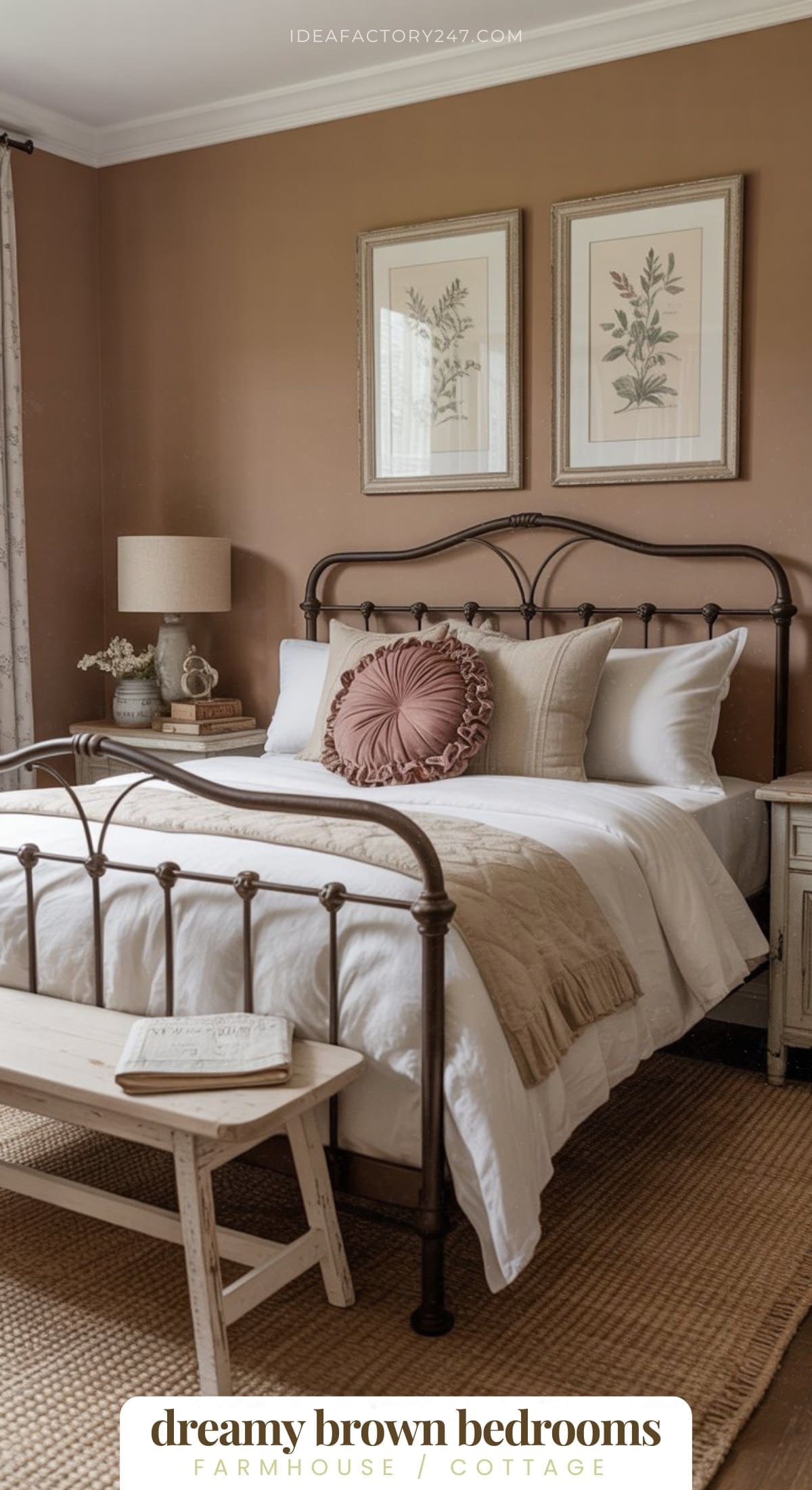 A cozy farmhouse-style bedroom with brown walls, a metal bed frame, white bedding with brown accents, a round decorative pillow, two botanical prints above the bed, a nightstand, lamp, and a small bench at the foot of the bed.