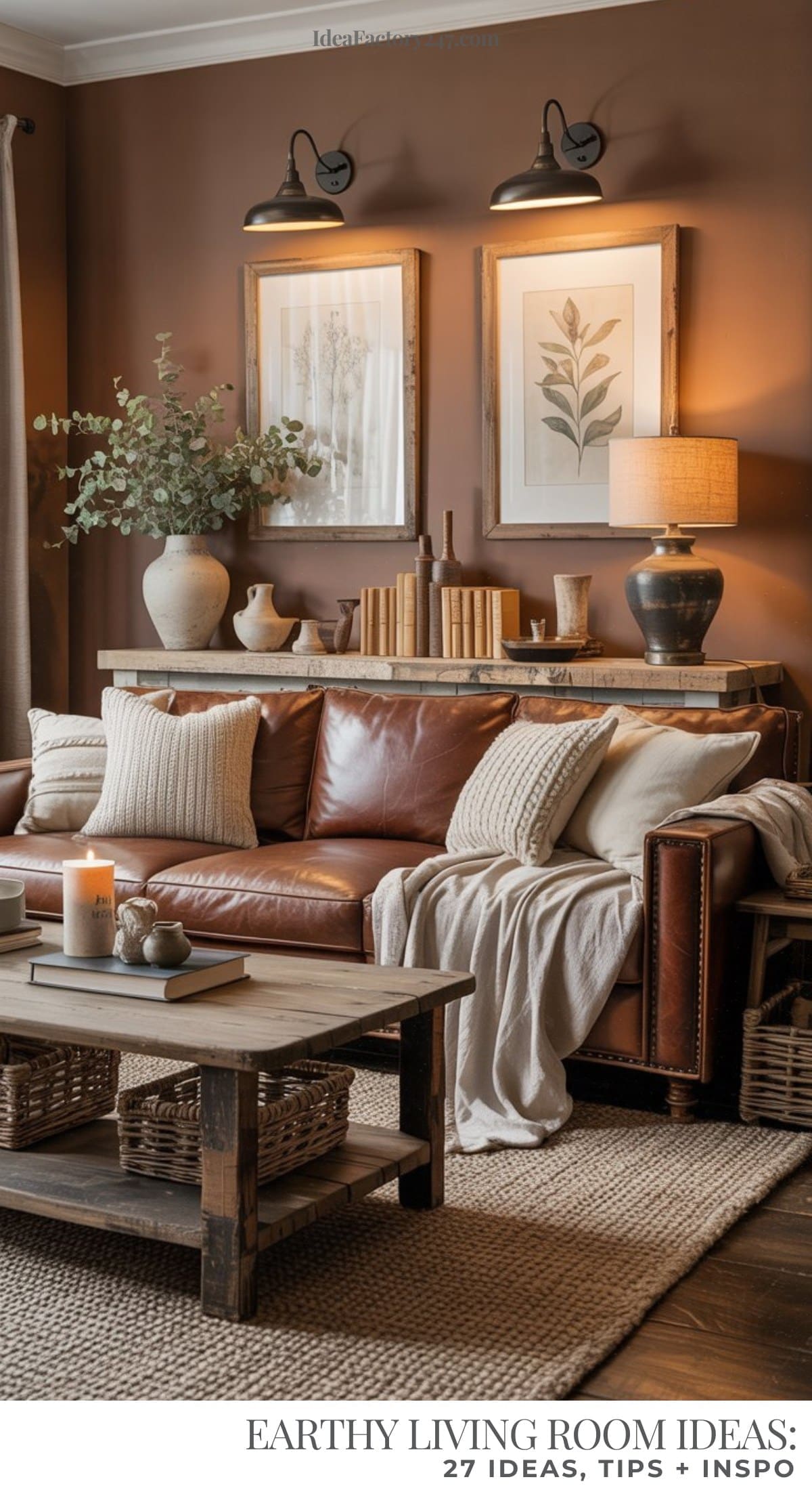 A cozy, earthy living room with a brown leather sofa, neutral pillows, a wooden coffee table, and rustic decor. Artwork, books, and greenery adorn a wooden console against a warm brown wall under two mounted lights.