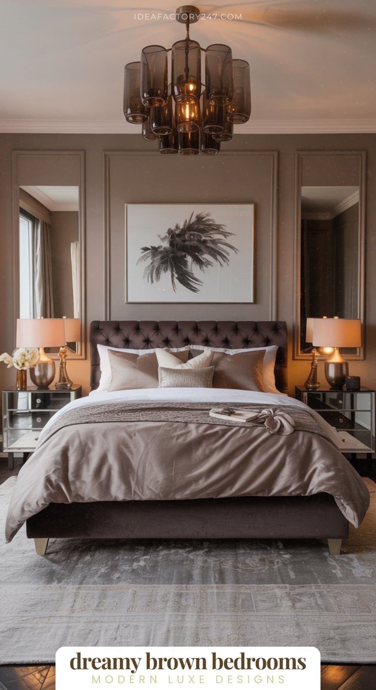A modern bedroom features a tufted brown bed with beige bedding, mirrored nightstands, gold lamps, and a framed palm leaf artwork above the bed. A large, dark chandelier hangs from the ceiling.