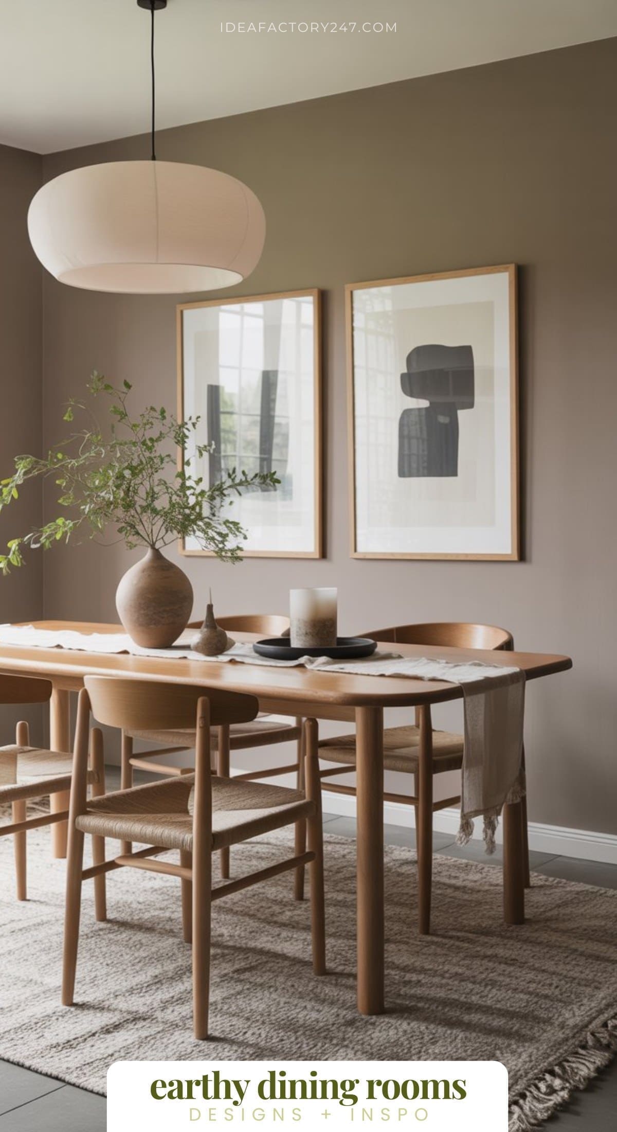 A modern earthy dining room with a light wooden table and chairs, neutral walls, two abstract framed artworks, a large pendant light, a vase with greenery, and a textured rug creates an inviting, minimalist atmosphere.