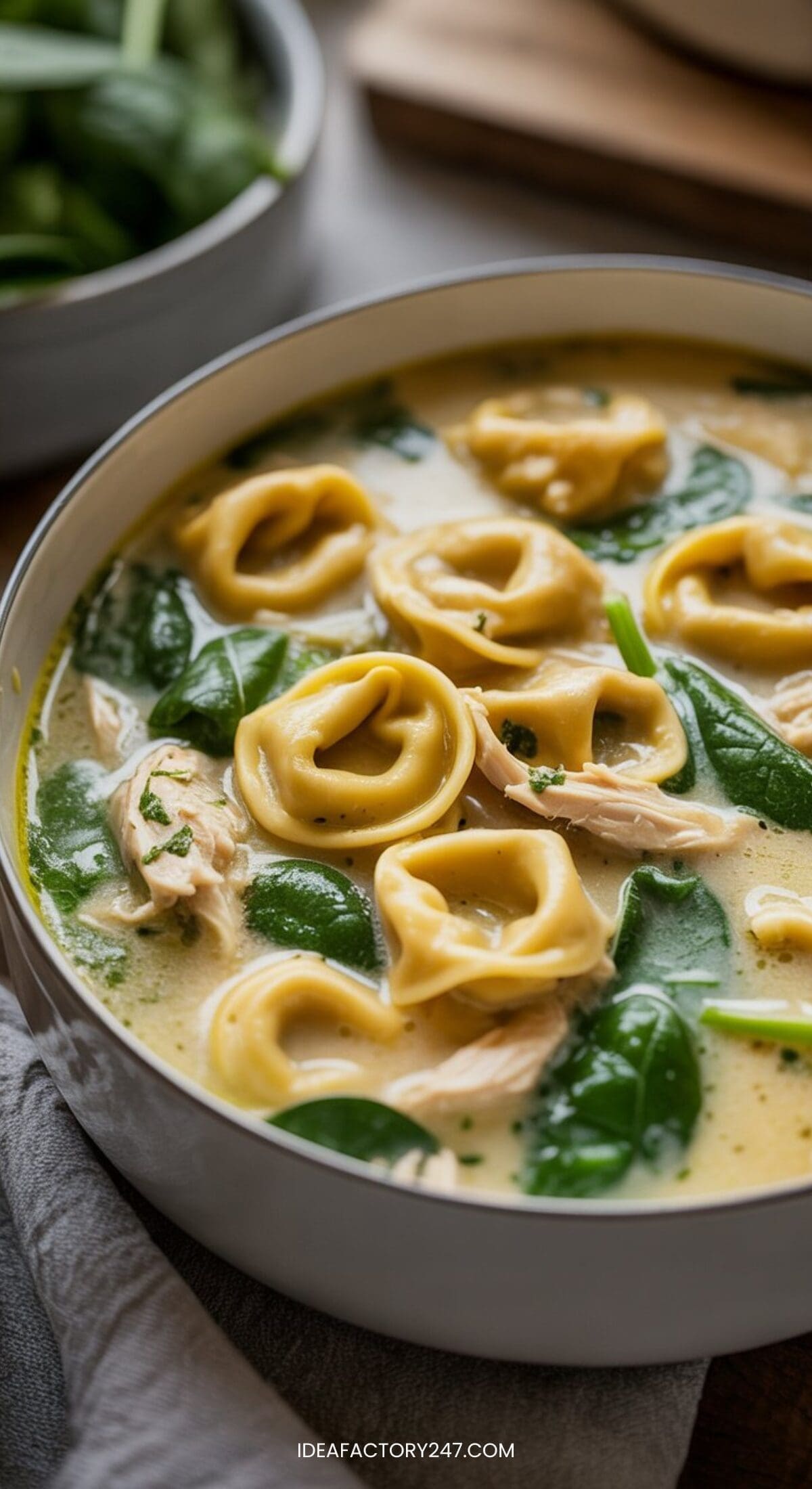 A bowl of creamy tortellini soup with spinach and shredded chicken, garnished with herbs. Rich and hearty, this dish is perfect for fans of crockpot soup recipes, featuring tender pasta and vibrant green spinach leaves.