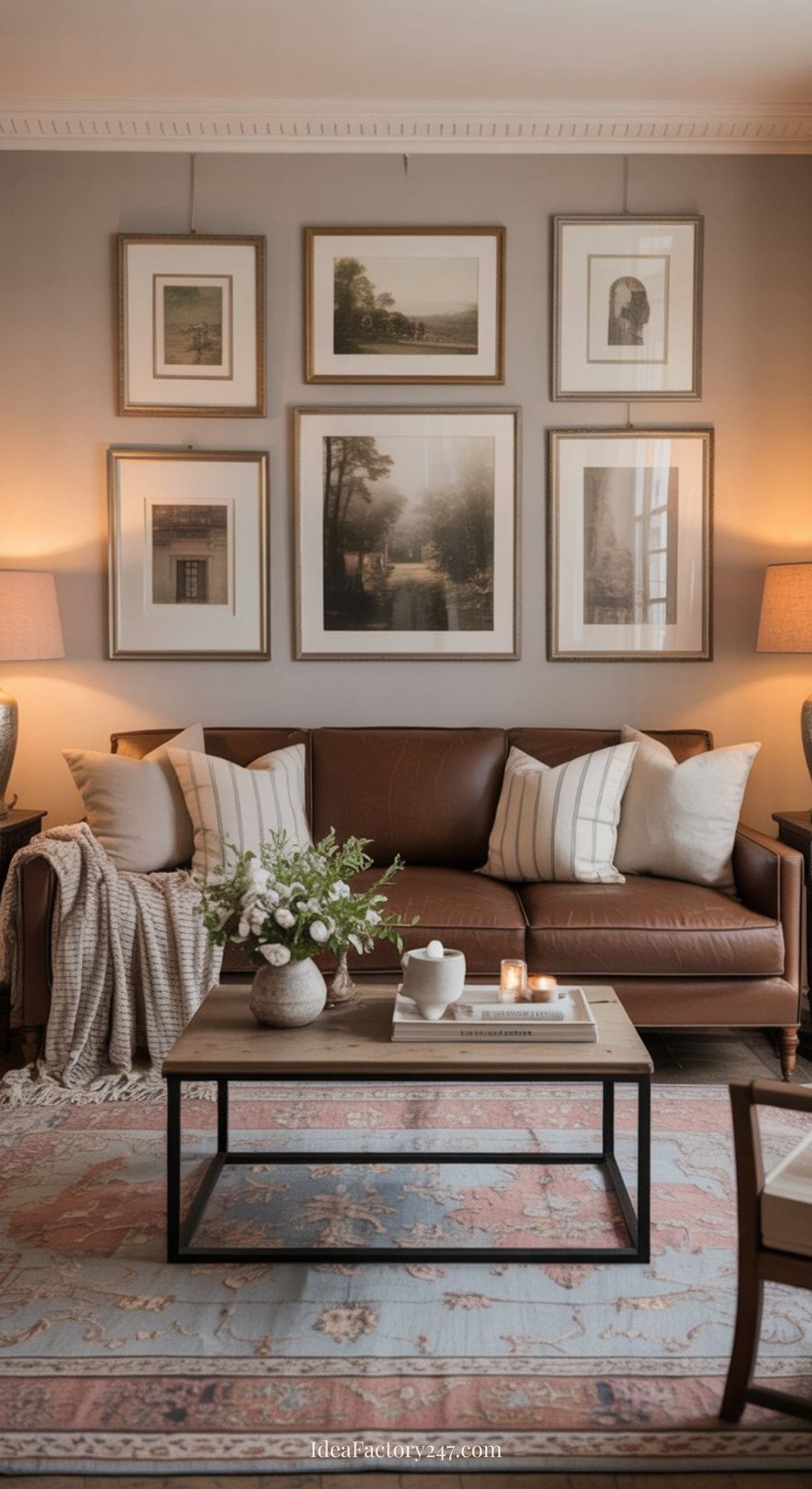 A cozy living room with a brown leather sofa, beige and striped pillows, a coffee table with flowers and candles, and framed art arranged in a gallery wall above the sofa. Warm lighting from two table lamps creates a welcoming atmosphere.