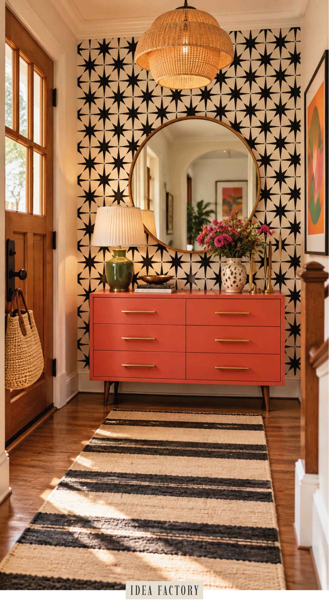 A coral six-drawer dresser sits against a star-patterned wallpaper wall in a colorful entryway, topped with a green lamp, a vase of flowers, and a round mirror.