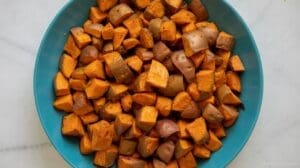 A blue bowl filled with seasoned, cubed sweet potatoes with cinnamon sits on a white marble surface.