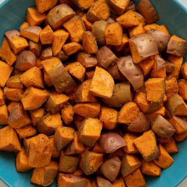 A blue bowl filled with seasoned, cubed sweet potatoes with cinnamon sits on a white marble surface.