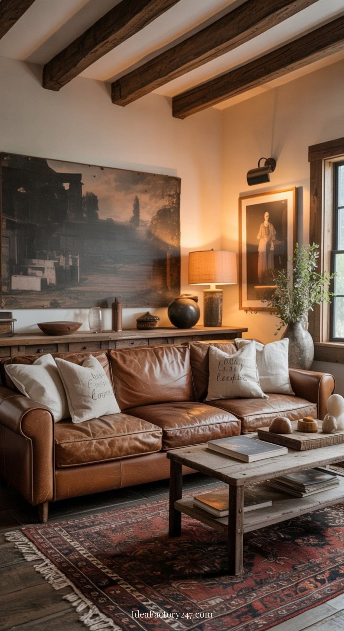 A cozy living room with a brown leather sofa, patterned rug, wooden coffee table, and framed art on the walls. Throw pillows and a large potted plant add warmth; soft, natural light streams in from a nearby window.