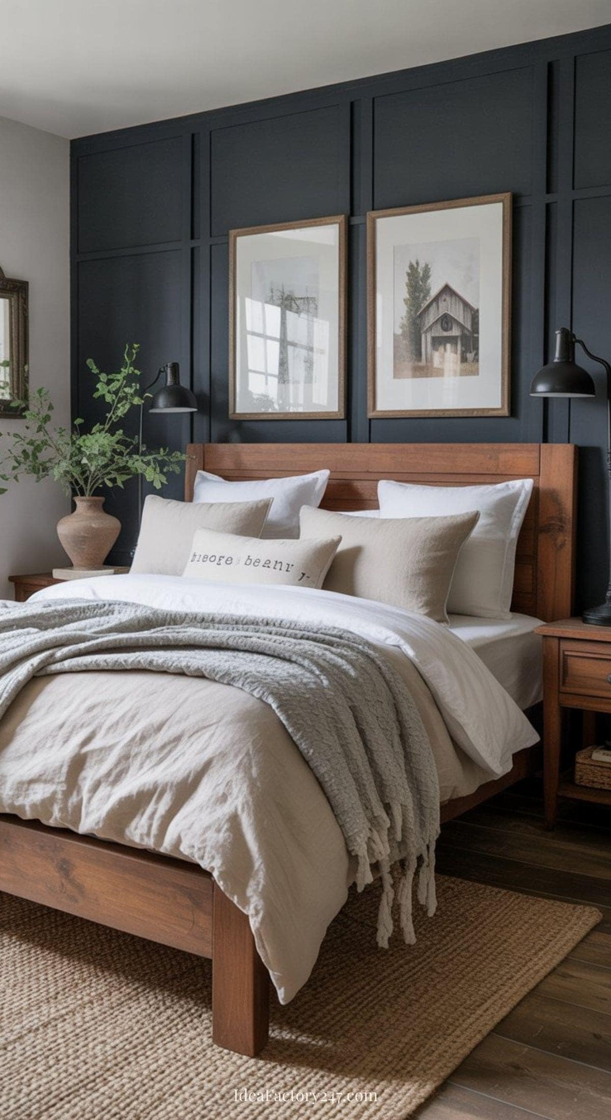A cozy bedroom with a wooden bed, neutral bedding, and gray knit throw blanket. Dark paneled accent wall features framed art. Nightstands with black lamps and a vase with greenery brighten the space.