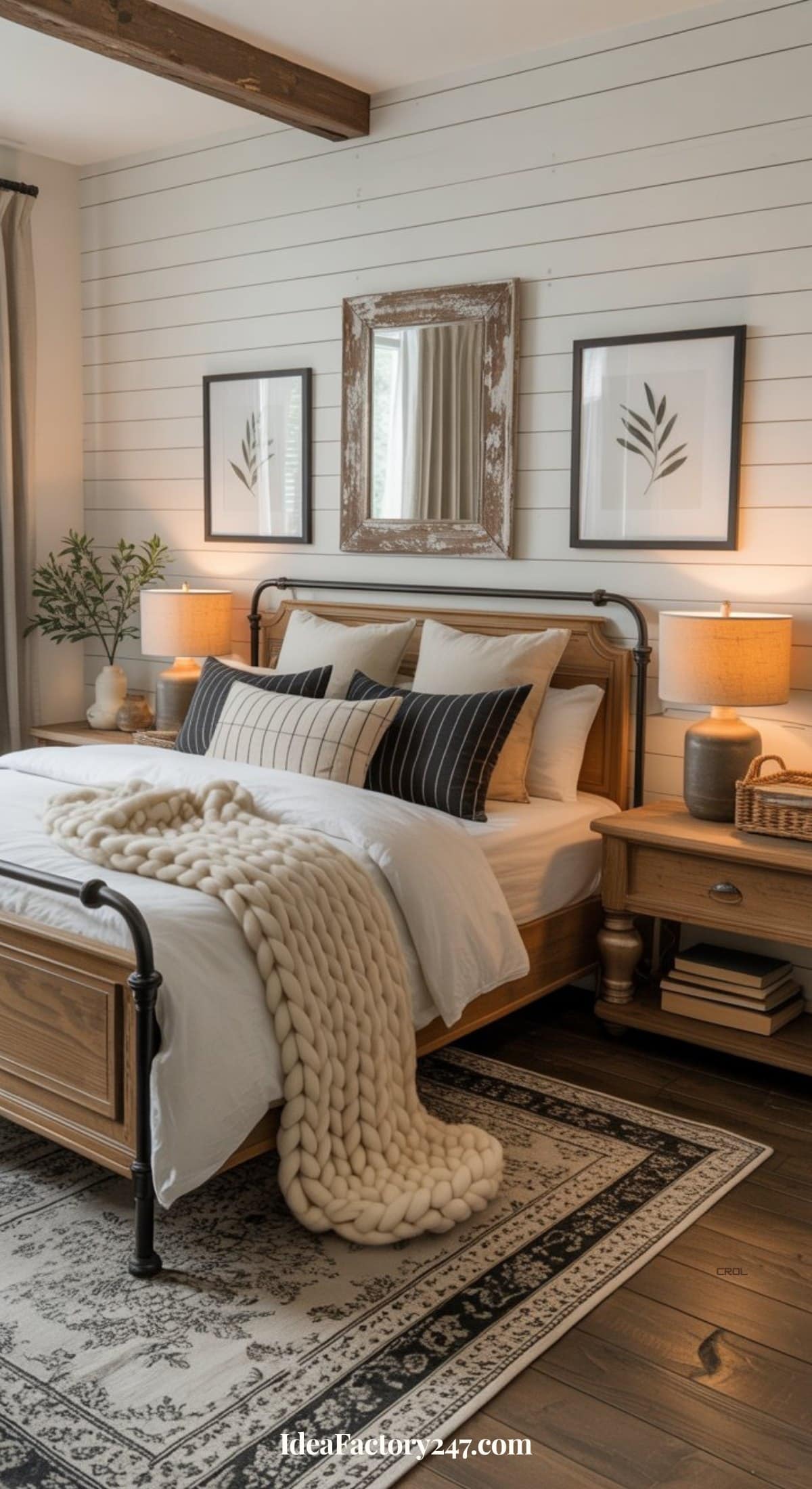 A cozy black and white bedroom with a wooden bed frame, white bedding, monochrome pillows, a chunky knit blanket, two bedside tables with lamps, framed artwork, a mirror, and a patterned rug on dark wood floors—perfect for black and white bedroom ideas.