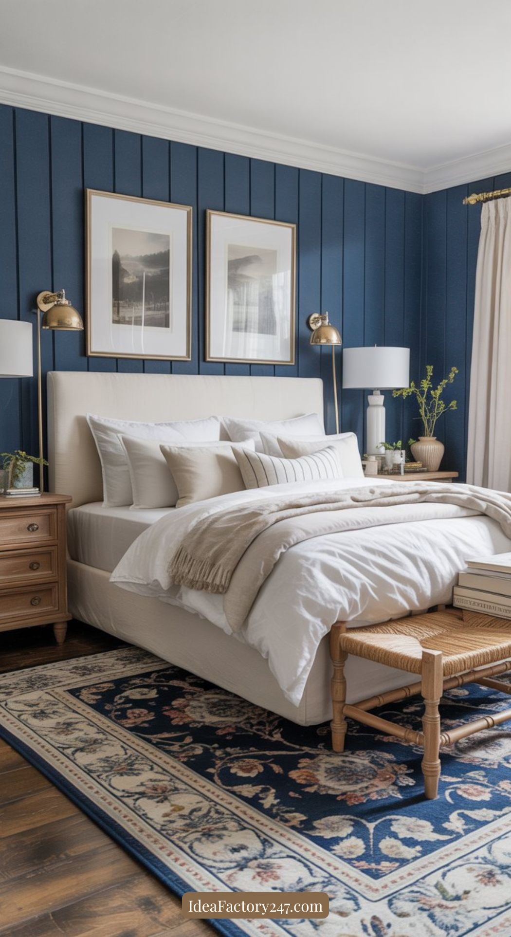 A cozy bedroom with a navy blue paneled accent wall, a beige upholstered bed with white bedding, matching nightstands, brass sconces, framed art, a patterned rug, and a wooden bench at the foot of the bed.