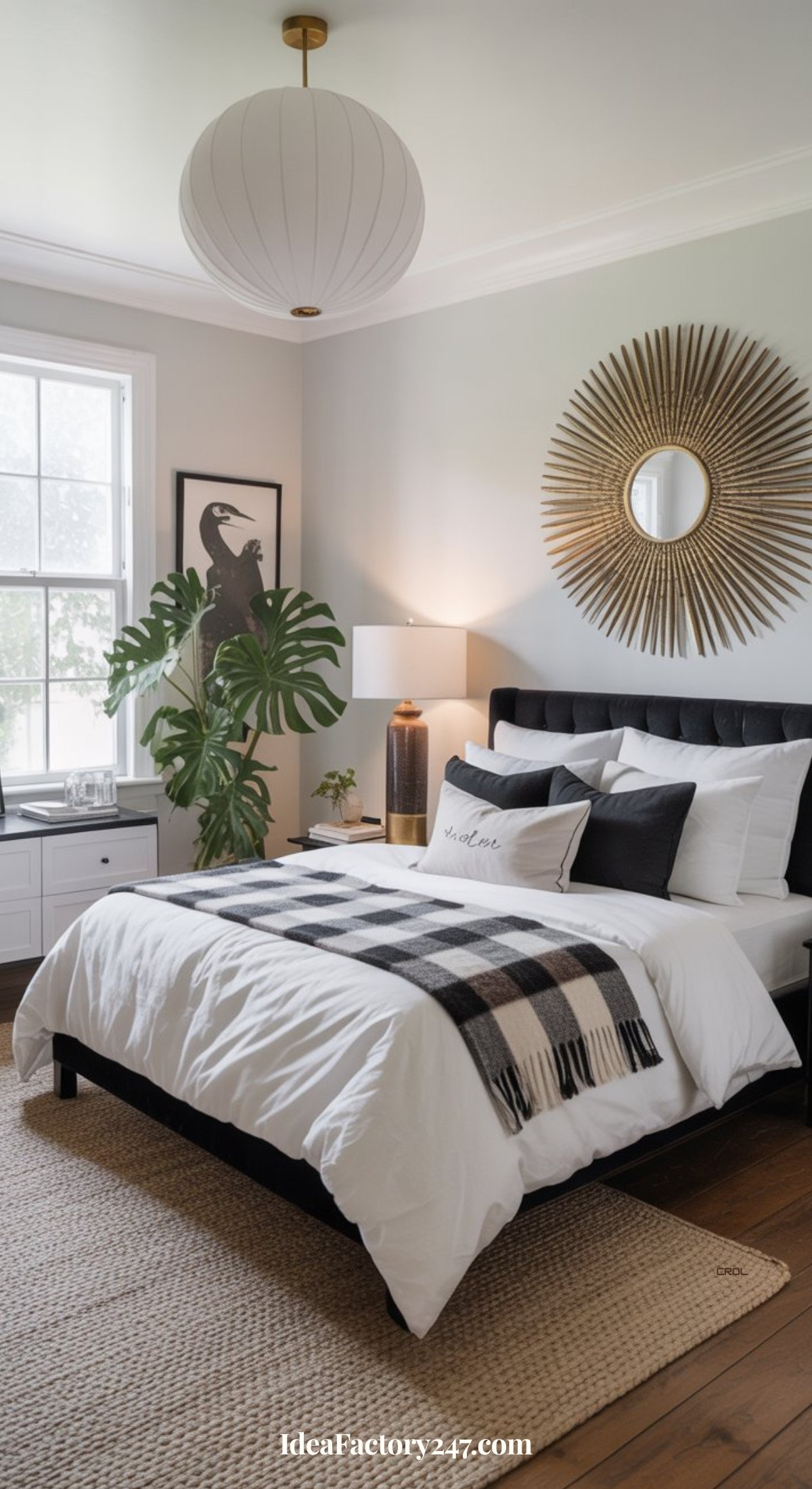 A modern bedroom featuring black and white bedroom ideas, with a neatly made bed, checkered blanket, sunburst mirror above the headboard, large leafy plant, bedside lamp, wall art, and a window flooding the space with natural light.