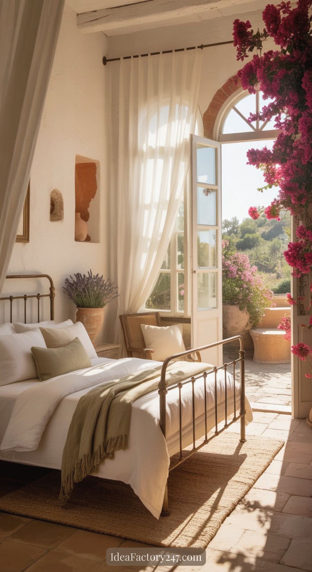 Bright, cozy bedroom with a metal bed, white linens, and green accents. Sunlight streams through an open door to a terrace with vibrant pink flowers and lush greenery—perfect for Mediterranean bedroom ideas.