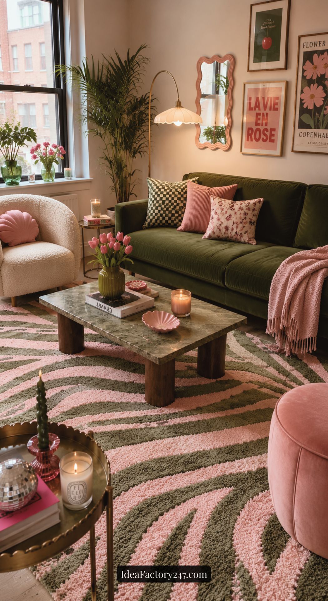 A stylish living room with a green velvet sofa, pink and green cushions, floral decor, pink candles, a wooden coffee table with flowers, and a pink and green zebra-patterned rug. Framed art hangs on the wall.