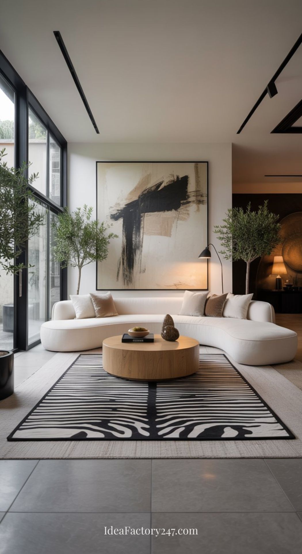 A modern living room with a curved white sofa, round wooden coffee table, black and white abstract rug, large abstract painting, floor lamp, potted trees, and floor-to-ceiling windows letting in natural light.