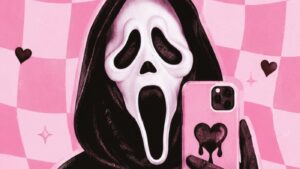 A person in a black hood wears a white “Scream” mask and holds a pink phone with a black heart on it, taking a selfie. The background is pink checkered with black hearts and sparkles.