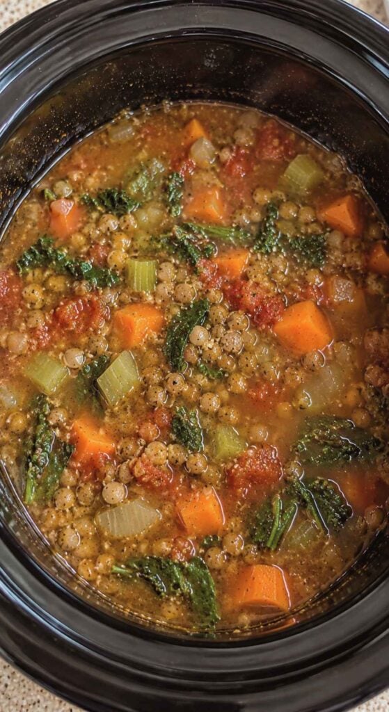 A close-up, overhead view of a healthy crockpot recipe consisting of lentil soup with carrots, celery, and kale.