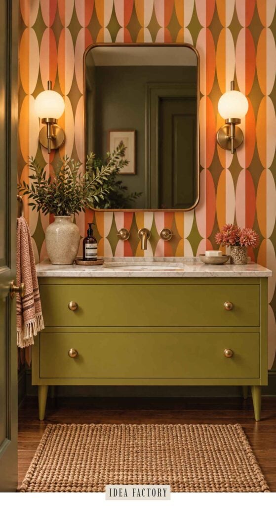 Bathroom vanity with a green cabinet, marble countertop, and a mirror against orange and olive geometric wallpaper.