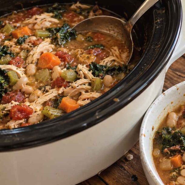 Slow cooker filled with chicken, white bean, and kale soup, next to a bowl of this healthy crockpot recipe.