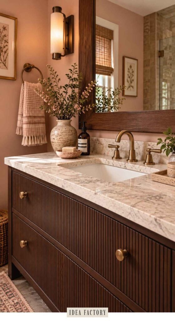 Bathroom vanity with a marble countertop, brass faucet, and fluted dark wood cabinets against a mauve wall.