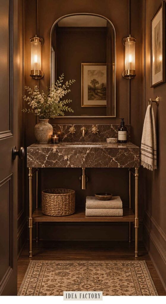 A dark brown bathroom vanity with a marble countertop, brass fixtures, a mirror, and a shelf holding folded towels and a woven basket.